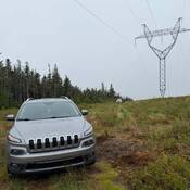 Un VUS Jeep gris garé au pied de lignes électriques et, au loin, un véhicule de police identifié.