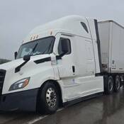 Un semi-remorque Freightliner blanc partiellement hors de la chaussée et la remorque blanche qui y est attelée bloquent entièrement l’une des deux voies de circulation.
