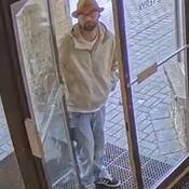 Photo d’un homme ayant une barbe brun pâle et portant des lunettes à monture foncée, un haut blanc, une veste havane, un jean bleu pâle, des chaussures noires et blanches, ainsi qu’un chapeau mou jaune moutarde
