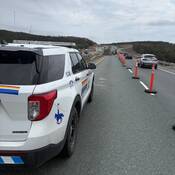 Véhicule de police identifié à la GRC garé dans une zone de travaux routiers, des véhicules circulant sur la voie de droite et des travailleurs à l’arrière-plan.