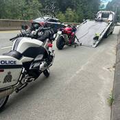 Une moto sportive rouge est chargée sur une dépanneuse sur la route 99, et une moto de la Patrouille routière de la Colombie Britannique est garée au premier plan
