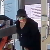 Femme vêtue de vêtements foncés, portant une casquette et des lunettes de soleil, et transportant un sac vert.