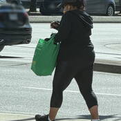 Femme, vue de dos, portant des vêtements foncés et portant un sac vert.
