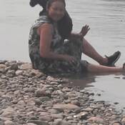 Karen Tessier assise dans l’eau. Elle porte une robe à motifs noirs et blancs et est accompagnée d’un petit chien noir.