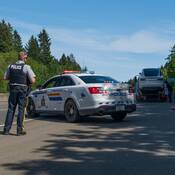 Un agent de la Patrouille routière de la Colombie Britannique, devant sa voiture de police, supervise le chargement d’une voiture de marque Tesla sur un camion de remorquage