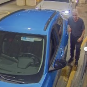 Un homme près de la portière côté conducteur d’un véhicule bleu, face à la caméra de surveillance.