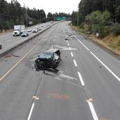 Une minifourgonnette de marque Kia, dont l’avant est considérablement endommagé, dans les voies en direction sud de la route 19 (Island Highway North), et une Volkswagen Jetta très endommagée dans le fossé, à l’arrière plan