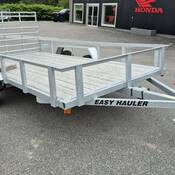 Photo d’une remorque utilitaire à essieux tandem en aluminium ou en argent, équipée d’un plancher en bois, dans un stationnement. Les mots « EASY HAULER » sont inscrits en lettres noires sur le côté de la flèche de la remorque.