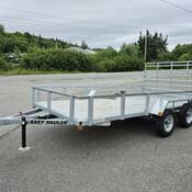 Photo d’une remorque utilitaire à essieux tandem en aluminium ou en argent, équipée d’un plancher en bois, dans un stationnement. Les mots « EASY HAULER » sont inscrits en lettres noires sur le côté de la flèche de la remorque.