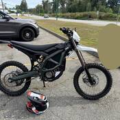 Une moto tout-terrain électrique garée à côté d’un véhicule de police banalisé et d’un casque dans un stationnement.