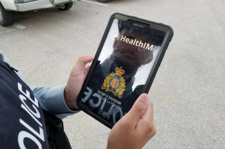 A male <abbr>RCMP</abbr> officer holding a tablet outdoors with his reflection visible on the screen.