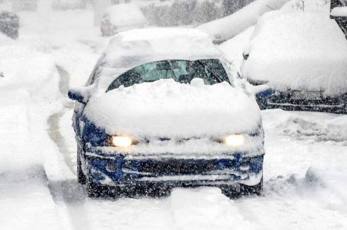 A snow-covered car drives on a snow-covered road. 