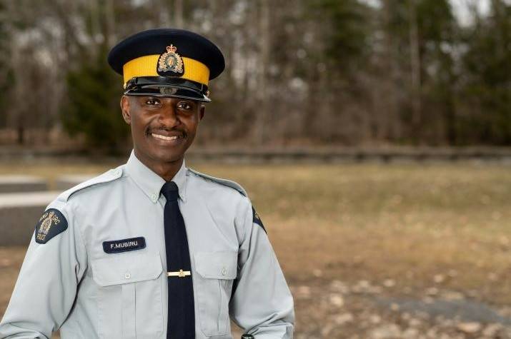 Black male <abbr>RCMP</abbr> officer stands outside smiling. 