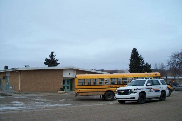 A yellow school bus is parked next to an RCMP vehicle outside of a school. 
