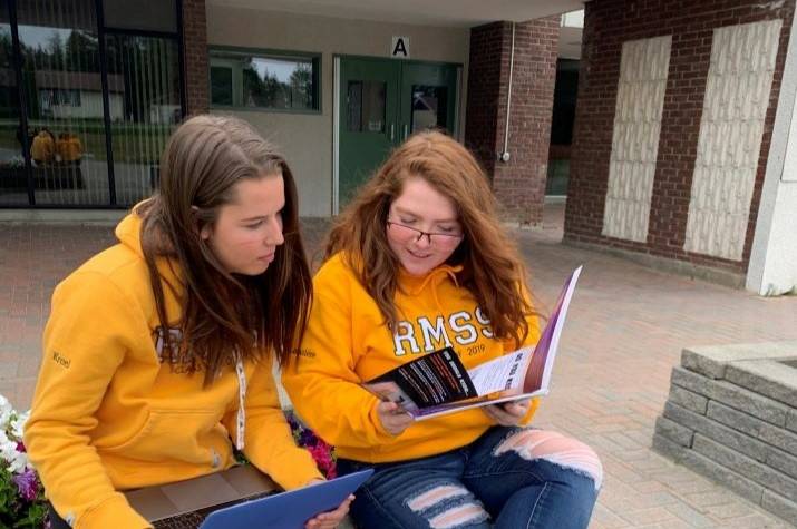 Two young women examine pamphlets while sitting on a bench.