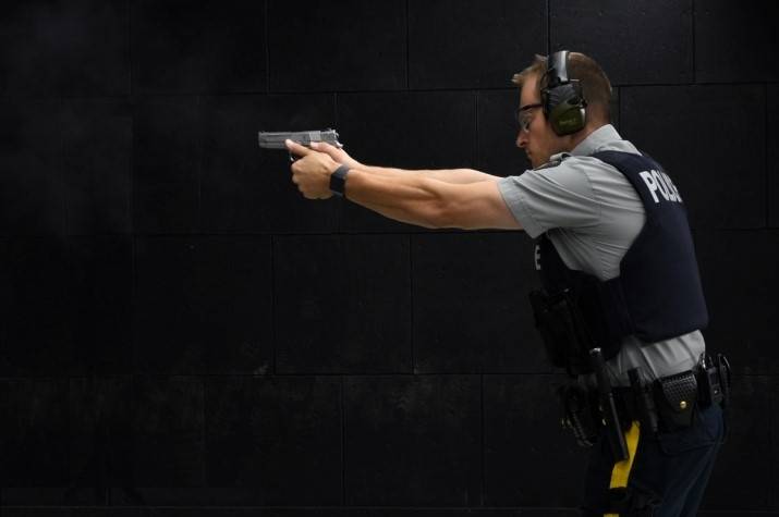 Male officer aims and points a pistol to the left in front of a dark background.
