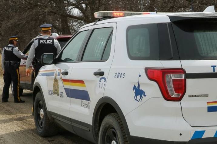 Male and female police officer stand on road beside car