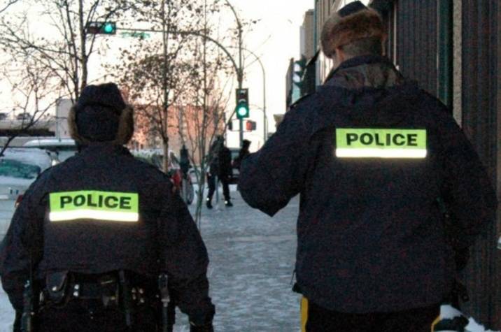 Two police officers walk on snowy sidewalk in city.