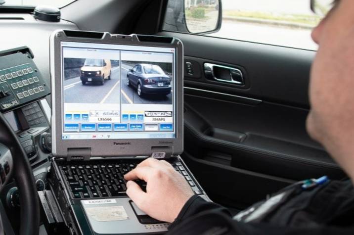 Police officer sits in police car looking at a computer screen.