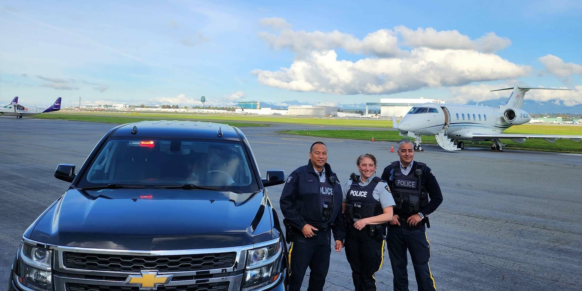 Des agents de la GRC de Richmond se tiennent debout à côté d’une camionnette et des avions sont en arrière-plan.