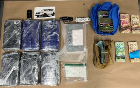 Evidence laid out on a table, including 6 bricks of cocaine, a vehicle key FOG, two knives, two other bags of drugs and multiple bundles of Canadian cash.
