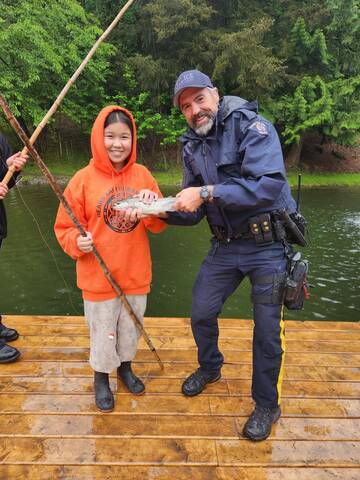 A police officer stands beside a student wearing an orange sweatshirt and holding a fish