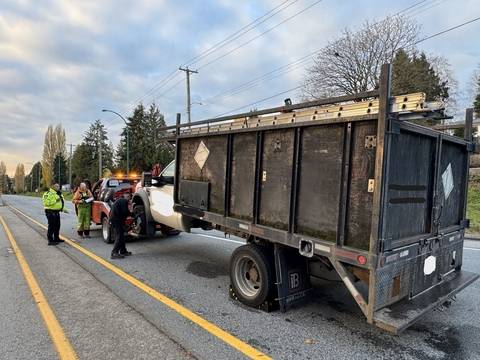 A black dump truck is being hooked up to a tow truck while a police officer wearing a yellow jacket stands by.