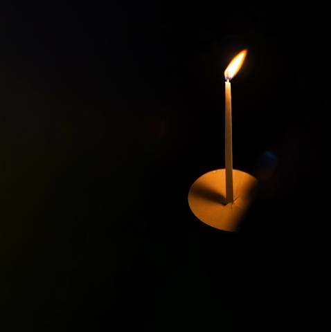 A single white candle with a flame on a dark background.