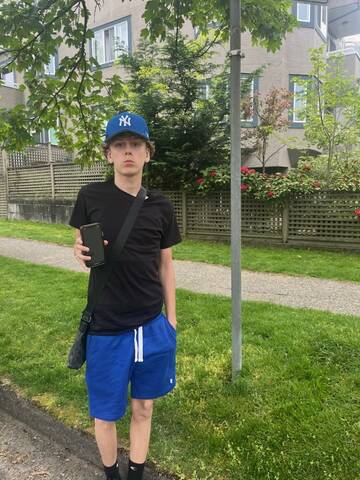 Boy with blue hat and shorts, with black t-shirt holding an iPhone