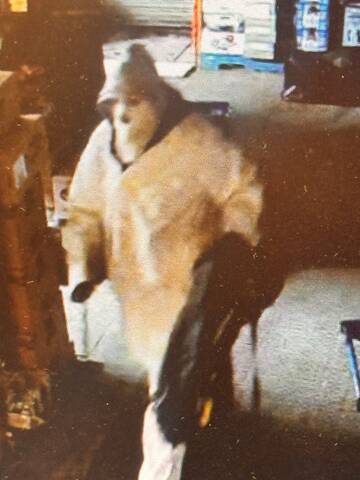 A still image of the suspect taken from video surveillance. The suspect is carrying a black duffle bag and is seen wearing a full-face mask, a white coat, white pants and has a hood up.