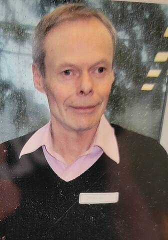 75-year-old man, brown sweater, pink and white shirt, grey hair.