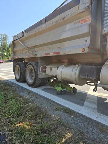 An officer dressed in yellow coveralls laying down under a dump truck on the side of the road completing an inspection.