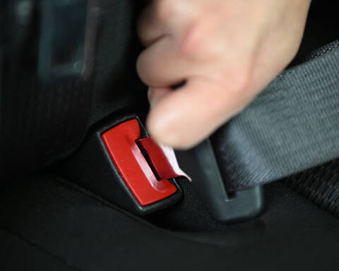 A hand buckling up their seatbelt in a car | Une main bouclant sa ceinture de sécurité dans une voiture.