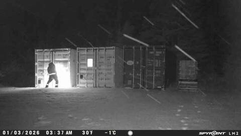 A person stands using a tool, attempting to break into a shipping container in the darkness. Sparks can be seen.
