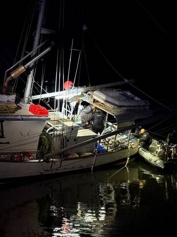 Two police officers with the suspect on board the fishing vessel in the water at night. Another officer is on a Zodiac-style beside the fishing vessel