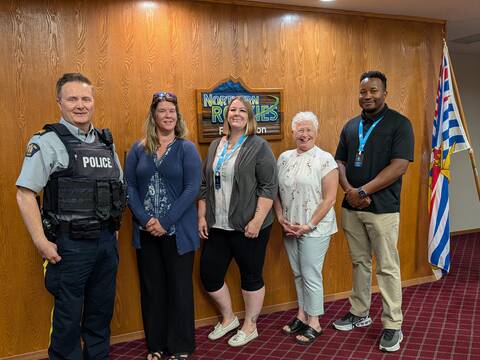 An RCMP officer in uniform stands indoors beside three women and a man who are all smiling