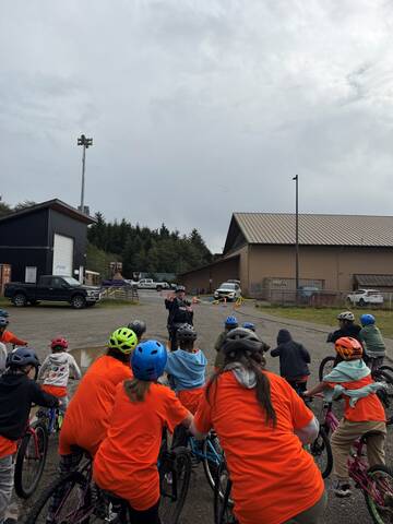 Photo of a Massett RCMP officer speaking to a group of Chief Matthews School students, who are all on bikes.