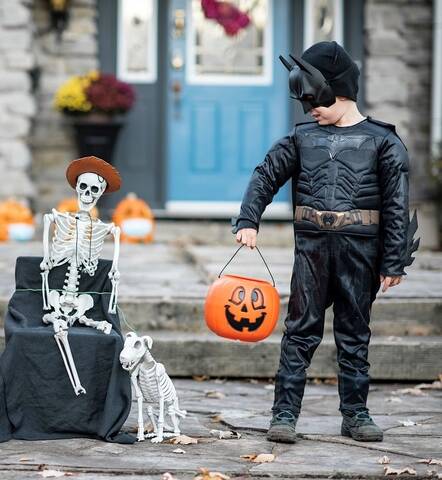 Photograph of a little boy in a Batman costume trick-or-treating by a skeleton