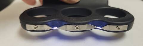 The bottom view of a rechargeable stun gun shaped like a pair of brass knuckles, and is comprised of plastic and metal. The stun gun is activated and arc's of voltage are visible