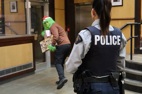 Police officer watching a person dressed as the grinch walk by with an arm full of presents.
