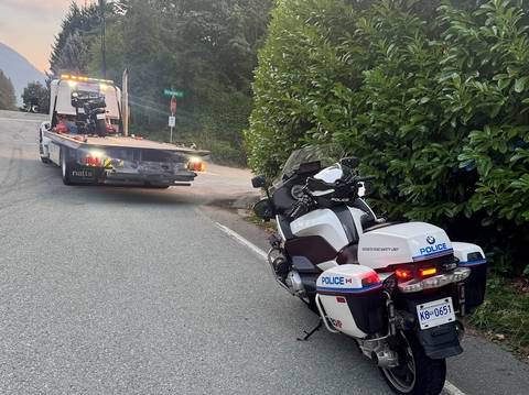 A Harley Davidson loaded onto a tow truck heading to a 30-day impound while a BC Highway Patrol motorcycle supervises