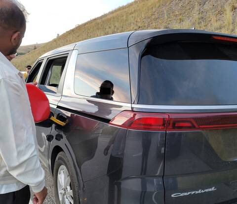 A grey minivan is refueled from a jerry can after running out of gas during a stop by BC Highway Patrol
