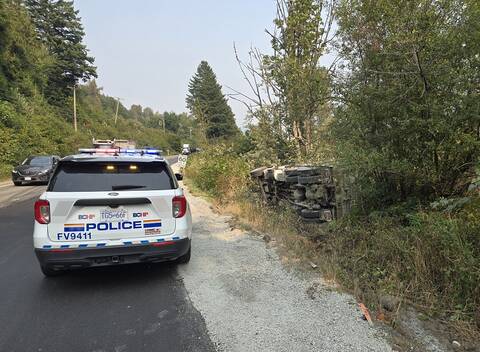 A BC Highway Patrol cruiser stopped behind a dump truck that rolled into a ditch on Lougheed Highway