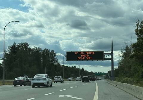 Cars drive along a highway under a sign that reads “BC Highway Patrol Ahead. Drive Safe”