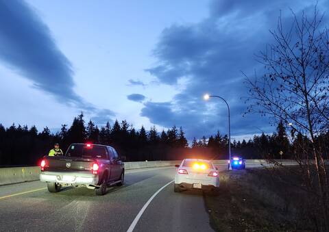 A BC Highway Patrol officer stops a truck at twilight with police cruisers at the side of the highway
