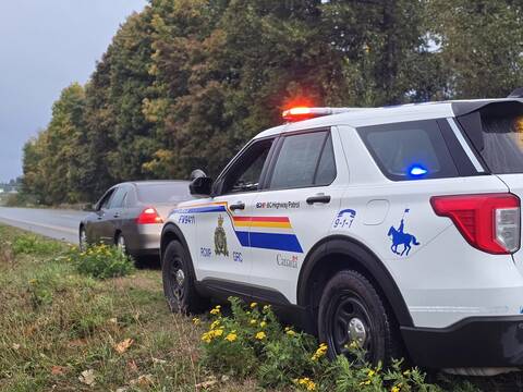 A BC Highway Patrol cruiser with its emergency lights on and a car pulled over at the side of the highway