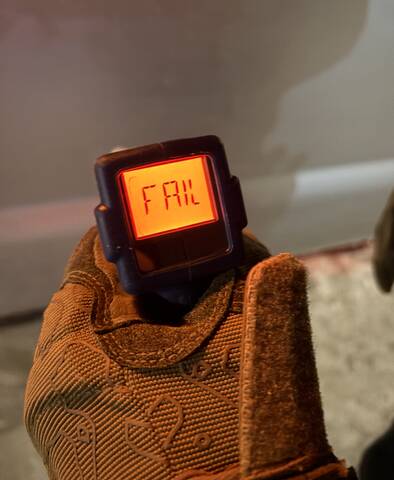 The display of a roadside screening device, being held by someone in brown mittens. The screen reads fail.