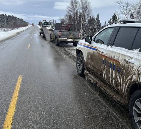 A truck being put onto the bed of a tow truck, with an RCMP police vehicle parked behind, on the shoulder of a roadway.