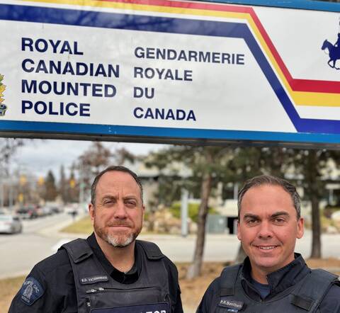 Staff Sgt. Bob Vatamaniuk and Sgt. Bentham standing in front of an RCMP sign wearing their blue crisis negotiation uniform.