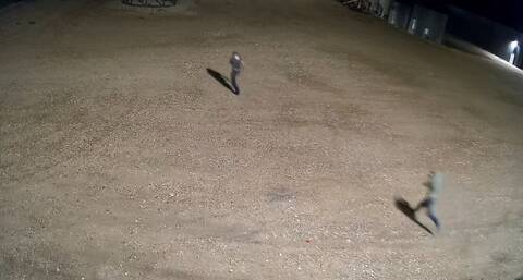 A screenshot that shows two individuals running across a large gravel area.